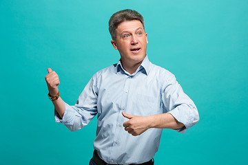 Image showing Beautiful male half-length portrait isolated on blue studio backgroud. The senior emotional surprised man