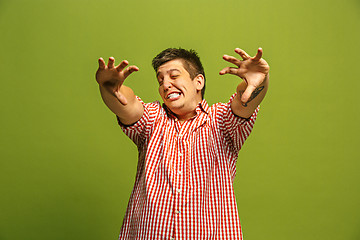 Image showing The young emotional angry man screaming on green studio background