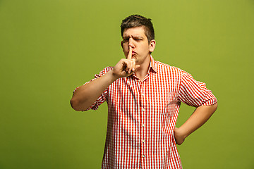 Image showing The young man whispering a secret behind her hand over green background