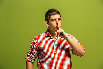 Image showing The young man whispering a secret behind her hand over green background