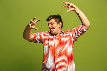 Image showing The young emotional angry man screaming on green studio background