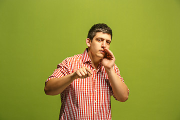 Image showing The young man whispering a secret behind her hand over green background