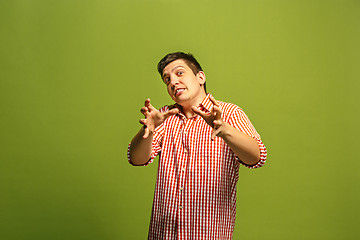 Image showing The young emotional angry man screaming on green studio background