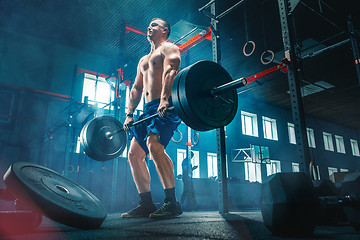 Image showing Fit young man lifting barbells working out in a gym