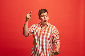 Image showing Beautiful male half-length portrait isolated on red studio backgroud. The young emotional surprised man