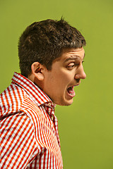 Image showing The young emotional angry man screaming on green studio background