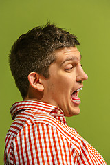 Image showing The young emotional angry man screaming on green studio background