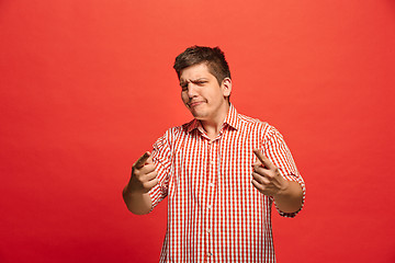 Image showing The young emotional angry man screaming on red studio background