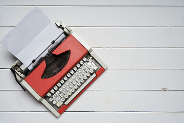 Image showing red vintage typewriter with white blank paper sheet on white wooden table