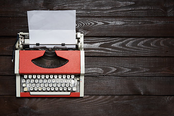 Image showing red vintage typewriter with white blank paper sheet on dark wooden table