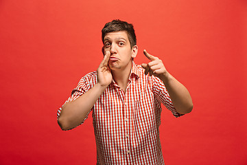 Image showing The young man whispering a secret behind her hand over red background