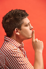 Image showing The young man whispering a secret behind her hand over red background