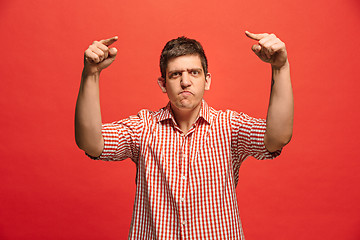 Image showing The young emotional angry man screaming on red studio background