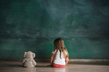 Image showing Little girl with teddy bear sitting on floor in empty room. Autism concept