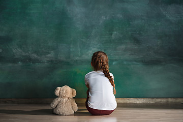 Image showing Little girl with teddy bear sitting on floor in empty room. Autism concept