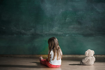 Image showing Little girl with teddy bear sitting on floor in empty room. Autism concept