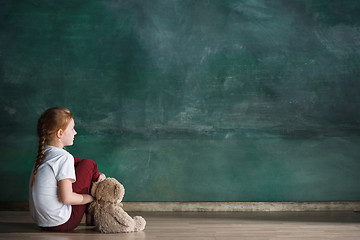 Image showing Little girl with teddy bear sitting on floor in empty room. Autism concept