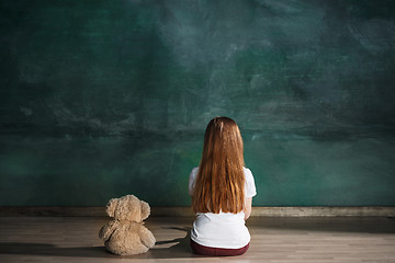 Image showing Little girl with teddy bear sitting on floor in empty room. Autism concept