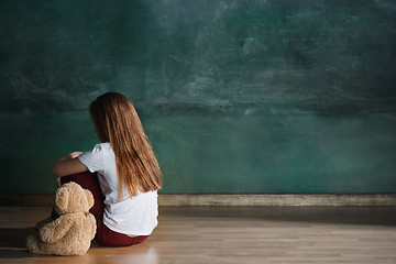 Image showing Little girl with teddy bear sitting on floor in empty room. Autism concept