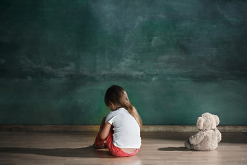 Image showing Little girl with teddy bear sitting on floor in empty room. Autism concept