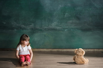 Image showing Little girl with teddy bear sitting on floor in empty room. Autism concept