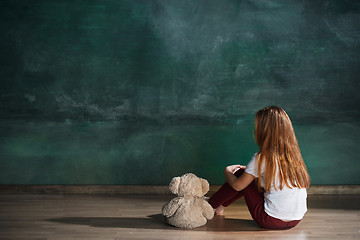 Image showing Little girl with teddy bear sitting on floor in empty room. Autism concept