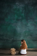 Image showing Little girl with teddy bear sitting on floor in empty room. Autism concept