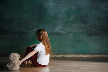 Image showing Little girl with teddy bear sitting on floor in empty room. Autism concept