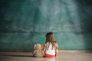 Image showing Little girl with teddy bear sitting on floor in empty room. Autism concept