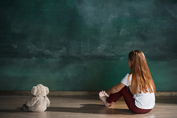 Image showing Little girl with teddy bear sitting on floor in empty room. Autism concept