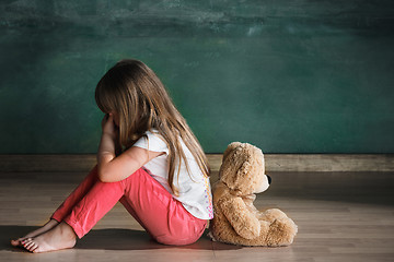 Image showing Little girl with teddy bear sitting on floor in empty room. Autism concept