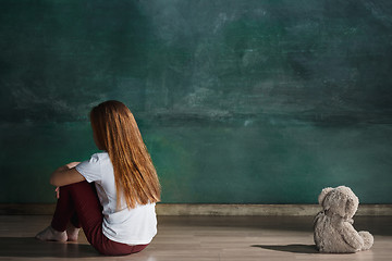 Image showing Little girl with teddy bear sitting on floor in empty room. Autism concept