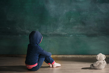 Image showing Little girl with teddy bear sitting on floor in empty room. Autism concept