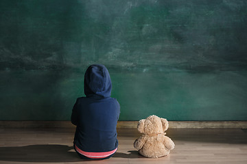 Image showing Little girl with teddy bear sitting on floor in empty room. Autism concept