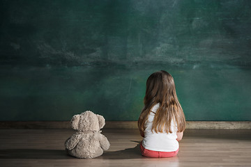 Image showing Little girl with teddy bear sitting on floor in empty room. Autism concept