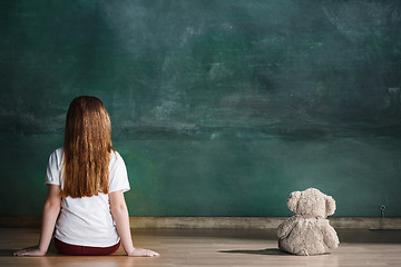 Image showing Little girl with teddy bear sitting on floor in empty room. Autism concept