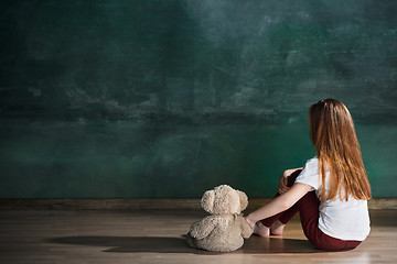 Image showing Little girl with teddy bear sitting on floor in empty room. Autism concept