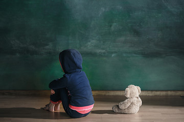 Image showing Little girl with teddy bear sitting on floor in empty room. Autism concept