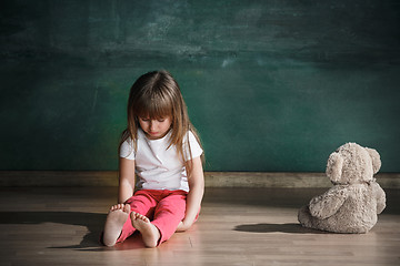 Image showing Little girl with teddy bear sitting on floor in empty room. Autism concept