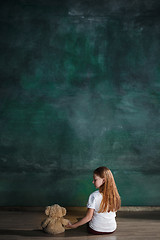 Image showing Little girl with teddy bear sitting on floor in empty room. Autism concept