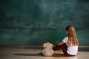 Image showing Little girl with teddy bear sitting on floor in empty room. Autism concept