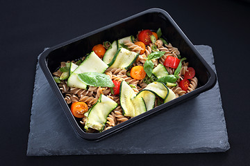 Image showing Dietary catering. Pasta salad with zucchini and tomatoes served on a black plate.