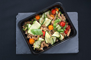 Image showing Box diet. Pasta salad with zucchini and tomatoes served on a black plate.