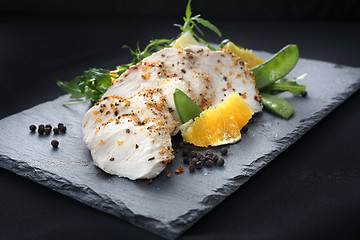 Image showing Poultry fillet on a salad with sugar peas and oranges on a black plate.