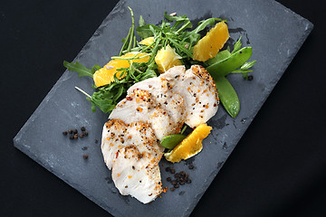 Image showing Poultry fillet on a salad with sugar peas and oranges on a black plate.