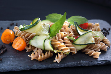 Image showing Pasta salad with zucchini and tomatoes served on a black plate.