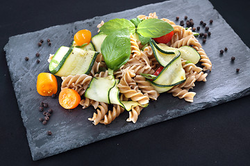 Image showing Spiral pasta with vegetables. Pasta salad with zucchini and tomatoes served on a black plate.