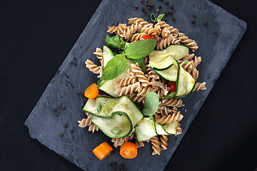 Image showing Pasta salad with zucchini and tomatoes served on a black plate.