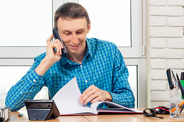 Image showing Joyful specialist in the office is talking on the phone and leafing through documents