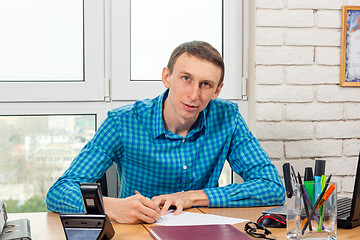 Image showing Young office specialist at the table signs the document